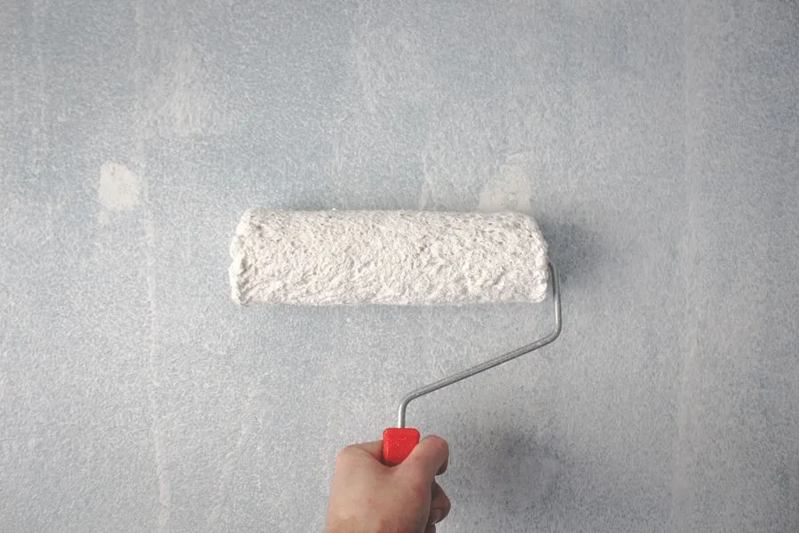 Paint roller applying white paint to a wall