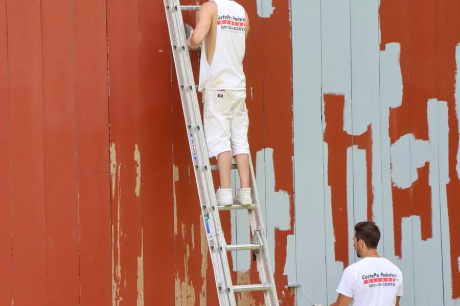 Painters repainting a timber exterior wall from a ladder